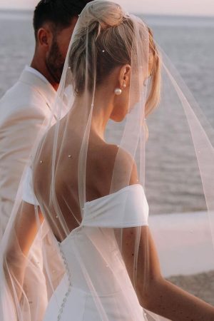 This dress rental is a dreamy off-the-shoulder wedding dress with a slit in front, made of crepe, a low back and cap sleeves