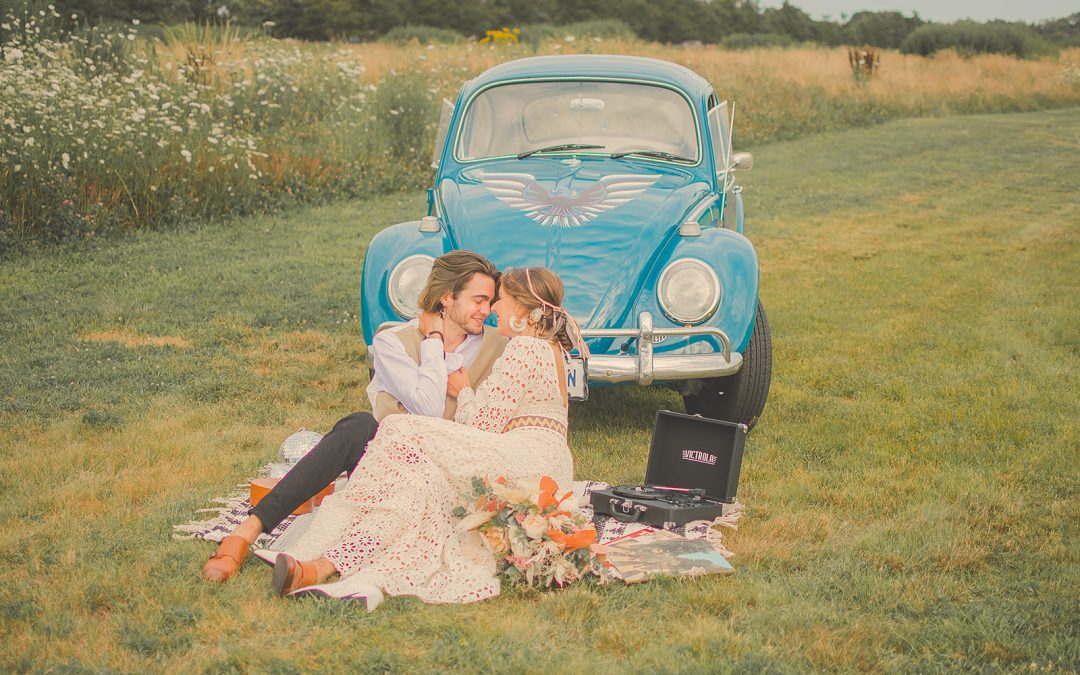 A blue "punchbuggy" with a couple sitting on the ground in front of it, snuggling